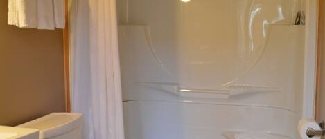 A bathroom with a shower enclosure, toilet, and a towel rack with folded towels.