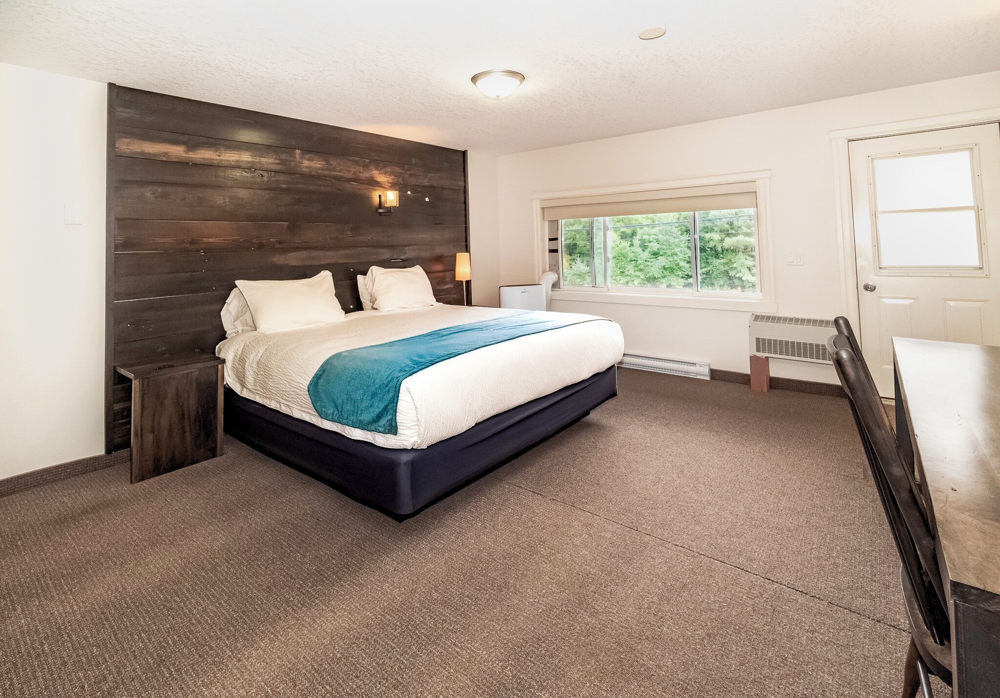 Un dormitorio con una cama grande, cabecera de madera, ventana con vistas y una puerta.