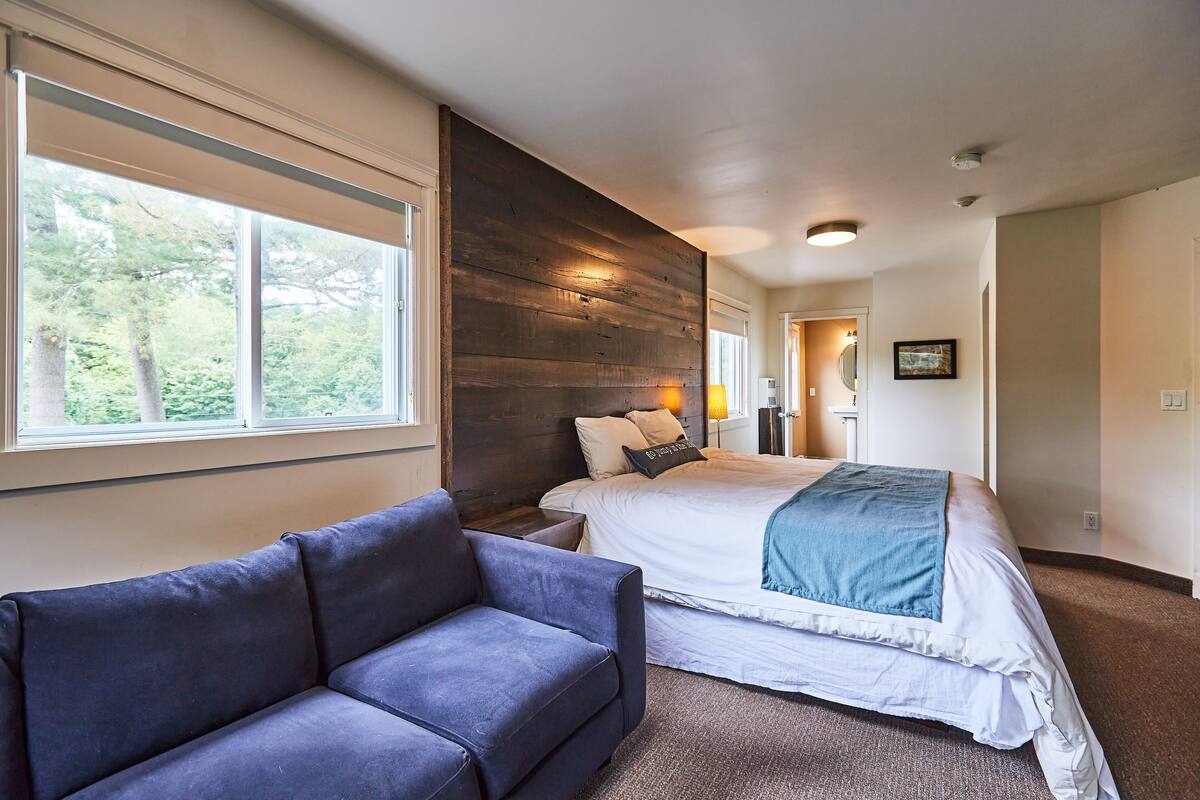 A bedroom with a large bed, a sofa, and a view of trees through the window.