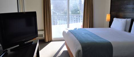 Una habitación de hotel con una cama, televisor, balcón con cortinas y una lámpara.