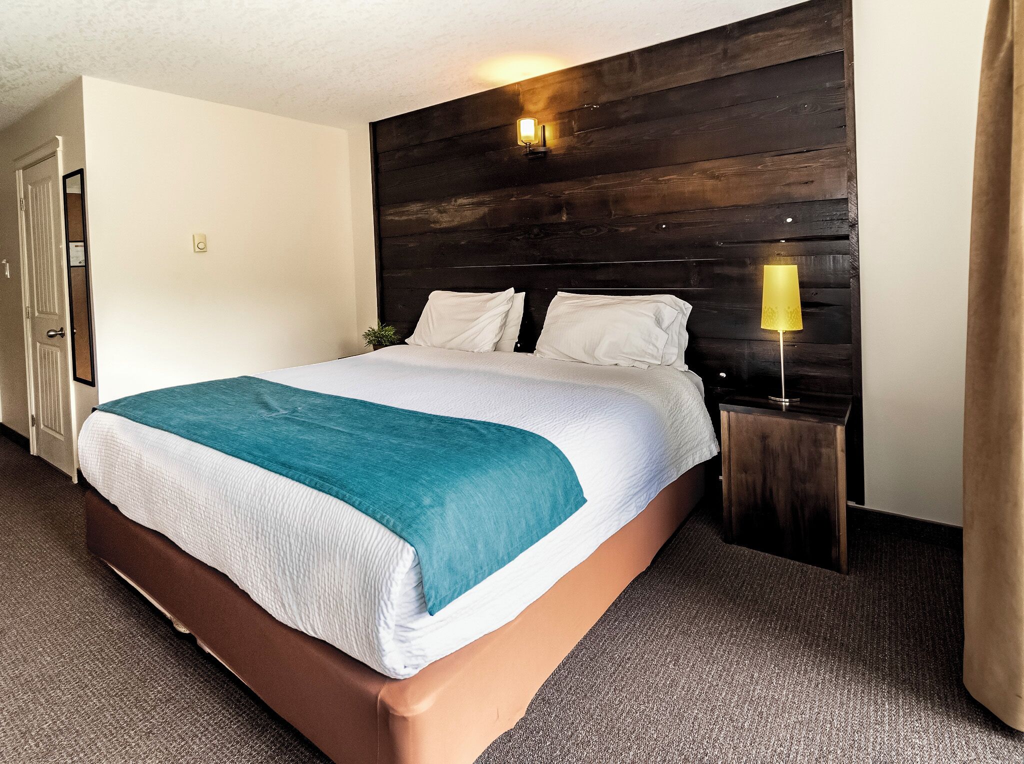 Ein Hotelzimmer mit einem großen Bett, einem Holzkopfstück, einer Nachttischlampe und einer kleinen Pflanze.