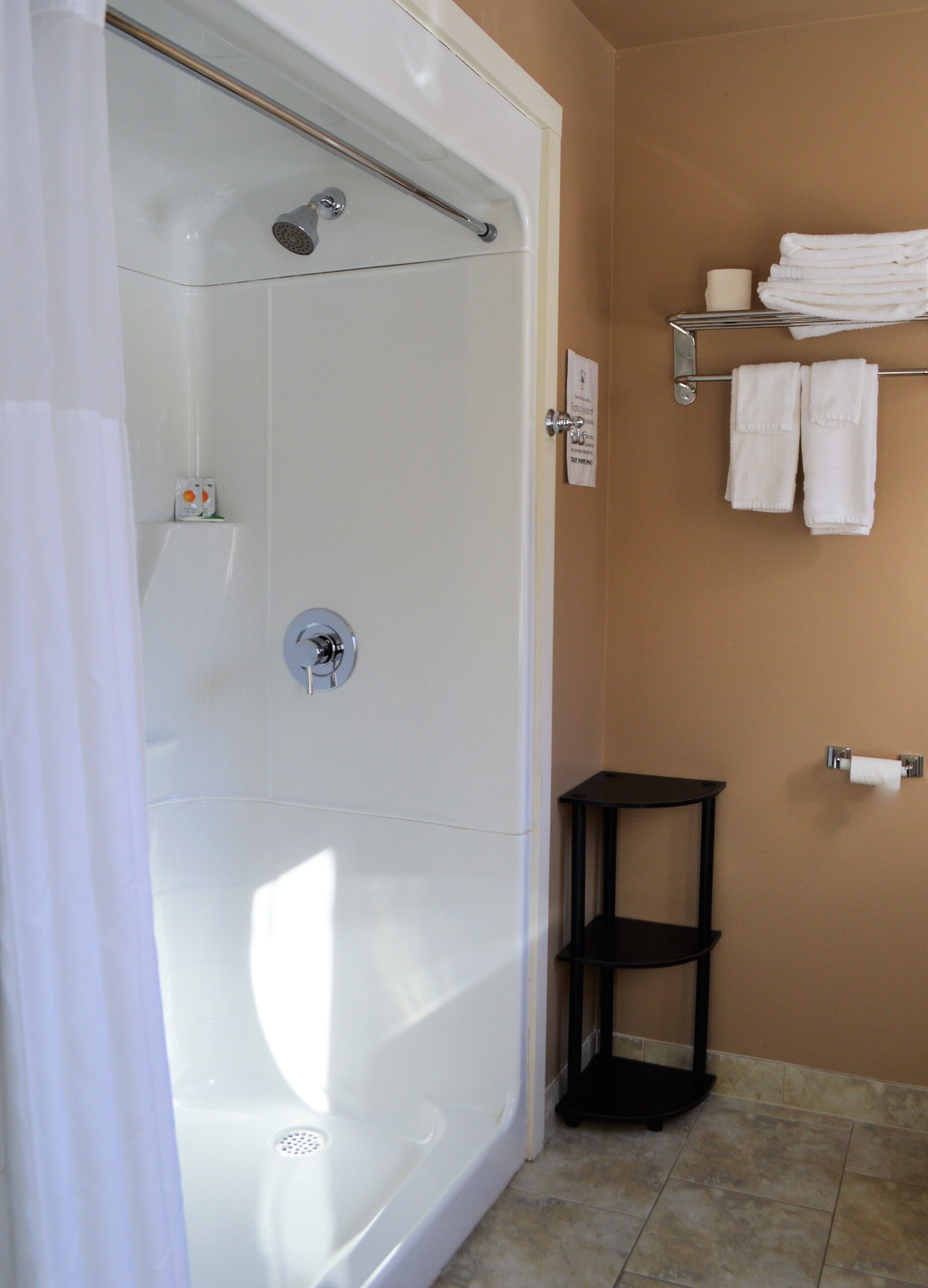 Un baño con ducha a nivel de suelo, un perchero con toallas dobladas, un dispensador de papel higiénico y un pequeño estante negro.