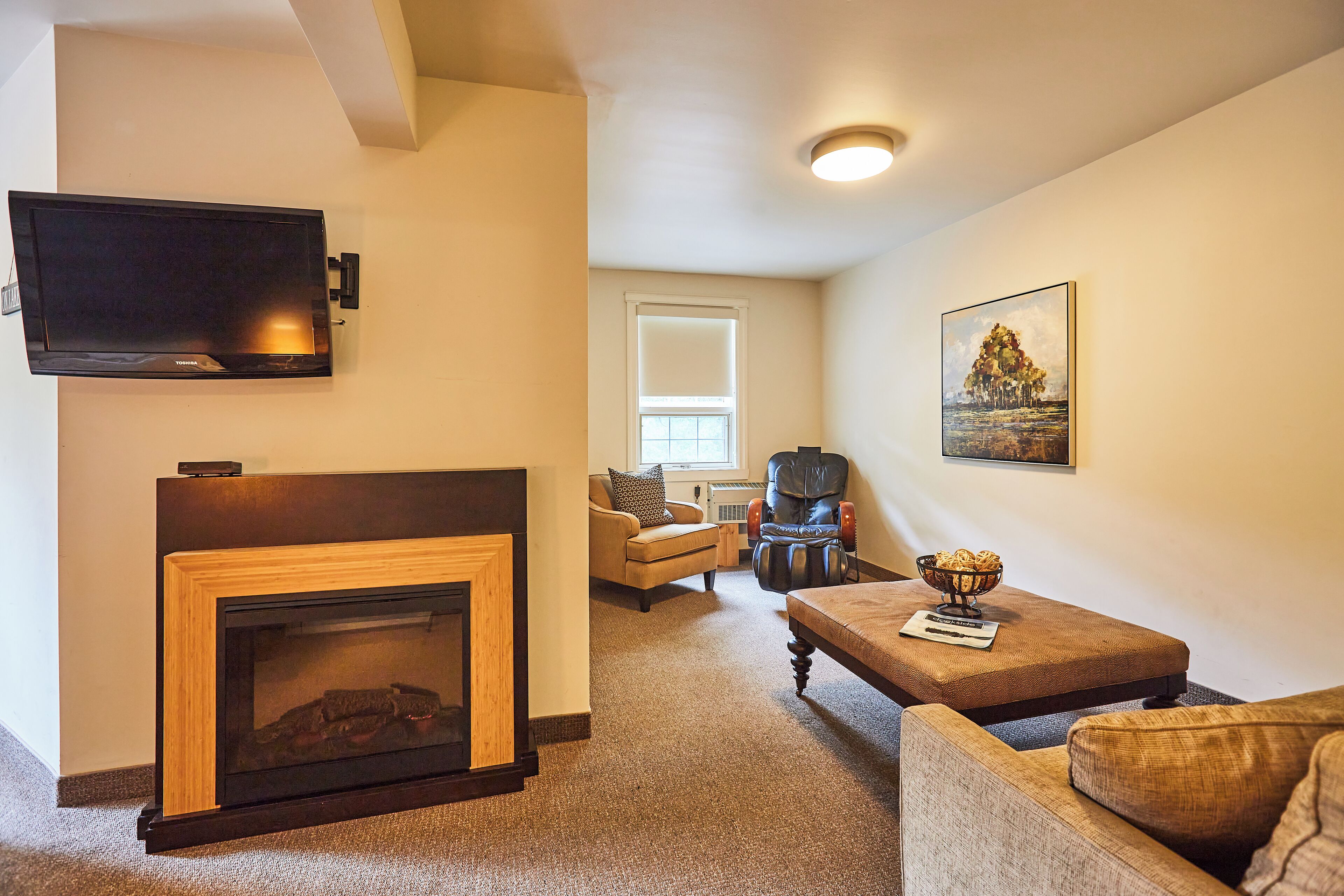 A living room with a fireplace, a television mounted on the wall, a comfortable sofa, and a chair.
