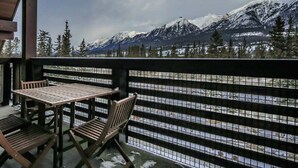 Una mesa y sillas de madera en un balcón con vista a montañas nevadas.