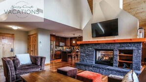 Amplia sala de estar con chimenea de piedra, muebles de madera y una cocina al fondo.