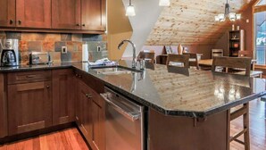 Una cocina con armarios de madera, encimera de granito, lavavajillas y un comedor con sillas y mesa de madera.