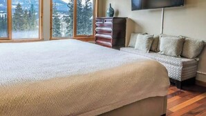 Un dormitorio con una cama grande, un aparador, un televisor y vistas a las montañas a través de amplias ventanas.