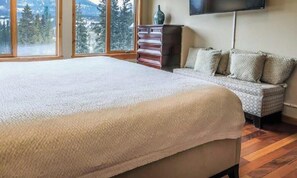 A bedroom with a large bed, a sofa, a dresser, and a TV mounted on the wall.