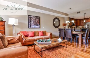 A modern living room with a brown leather sofa, a coffee table, and a dining area with wooden chairs and a table.