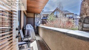 A balcony with a covered seating area, stone walls, and a view of neighboring houses. - Spring Creek Vacations 2 BR Premier Condo 115R (Canmore)