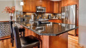 A modern kitchen with granite countertops, stainless steel appliances, and wooden cabinetry. - Spring Creek Vacations 2 BR Premier Condo 115R (Canmore)