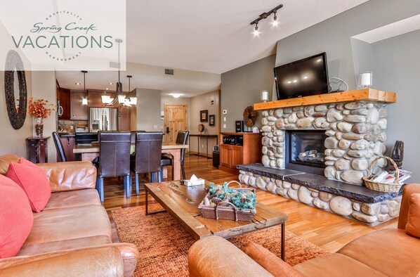 A spacious living room with a stone fireplace, leather sofas, and a dining area with a kitchen in the background.