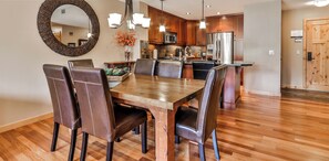 A spacious dining area with a wooden table and leather chairs, a kitchen with modern appliances, and a large mirror on the wall.