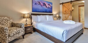 Une chambre d’hôtel avec un grand lit, une chaise, deux tables de chevet avec des lampes, une porte en bois et un tableau accroché au mur.