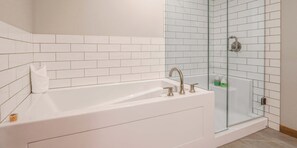 A modern bathroom with a white bathtub, a glass-enclosed shower, and white tiled walls. - Spring Creek Vacations 3 BR Premier Condo 103W (Canmore)