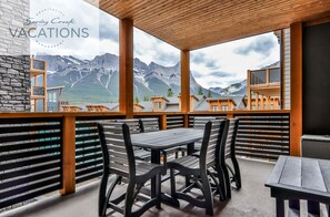 A balcony with wooden railings and tables, offering a view of mountains and other buildings.