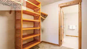 Quarto com uma estante de madeira na parede, uma porta que dá para outro espaço e um tapete pequeno no chão.