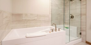 A modern bathroom with a glass-enclosed shower, a white bathtub, and a marble-tiled wall.