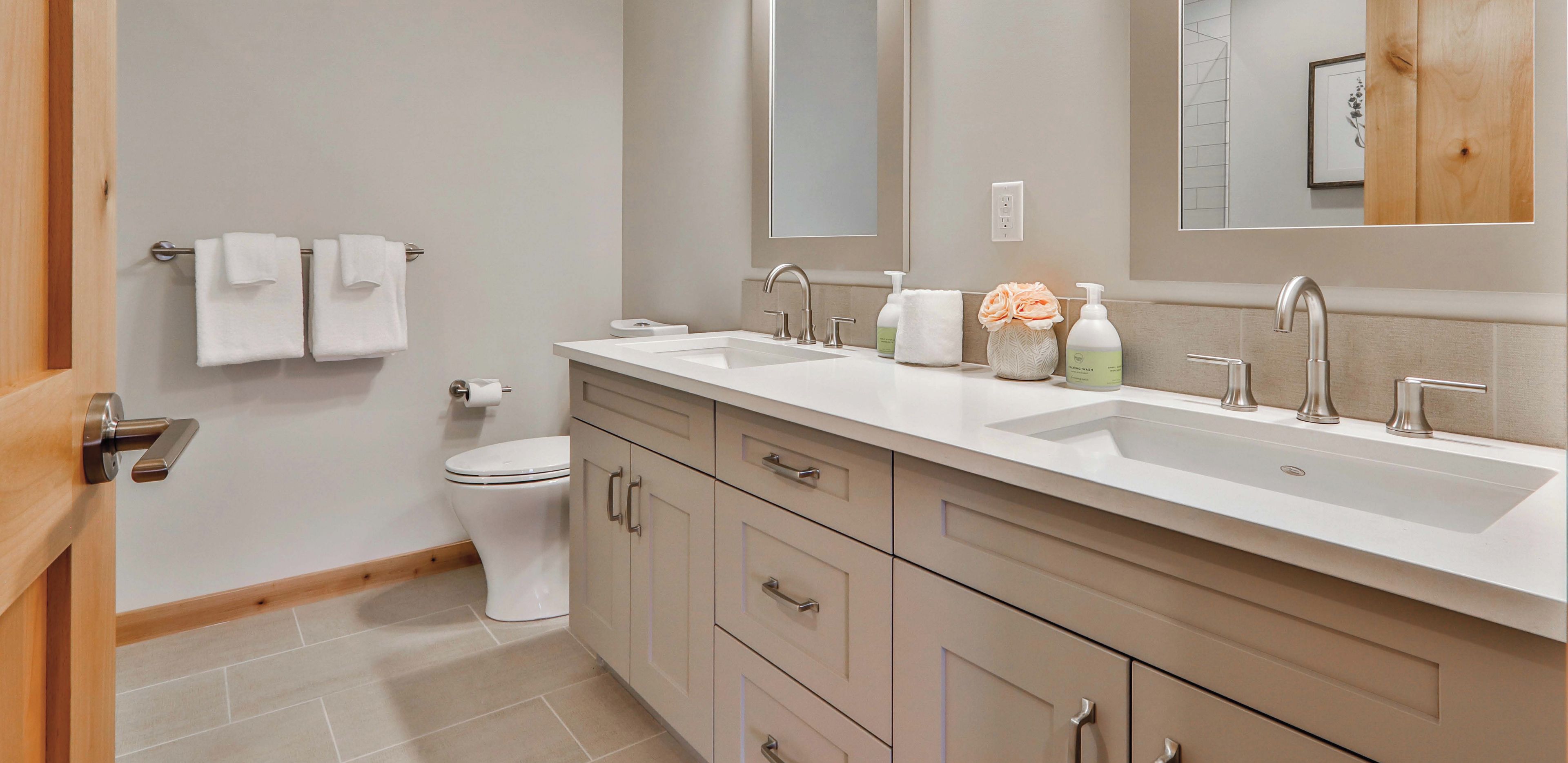A modern bathroom with a double sink, a large mirror, and a toilet.