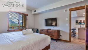 A bedroom with a large bed, wooden dresser, and a TV mounted on the wall.