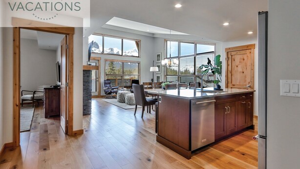 A spacious kitchen with wooden cabinets, a central island, and large windows offering mountain views. - Spring Creek Vacations 3 BR Premier Condo 309W (Canmore)