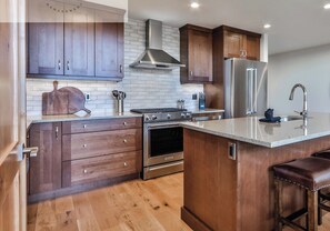 Une cuisine moderne avec des meubles en bois, des appareils électroménagers en acier inoxydable et une grande horloge au mur.