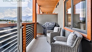 Un balcon doté de meubles en osier, d’un barbecue et offrant une vue sur les montagnes.