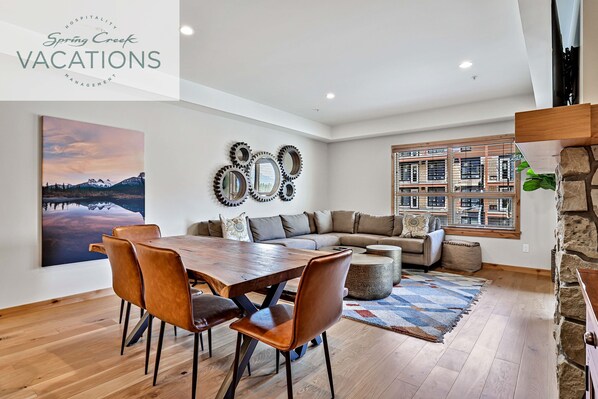 A spacious living area with a wooden dining table, leather chairs, a large sofa, and a stone accent wall.