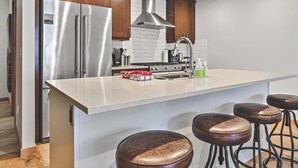 Une cuisine moderne dotée d’appareils électroménagers en acier inoxydable, de meubles en bois et d’un grand îlot central avec des tabourets.