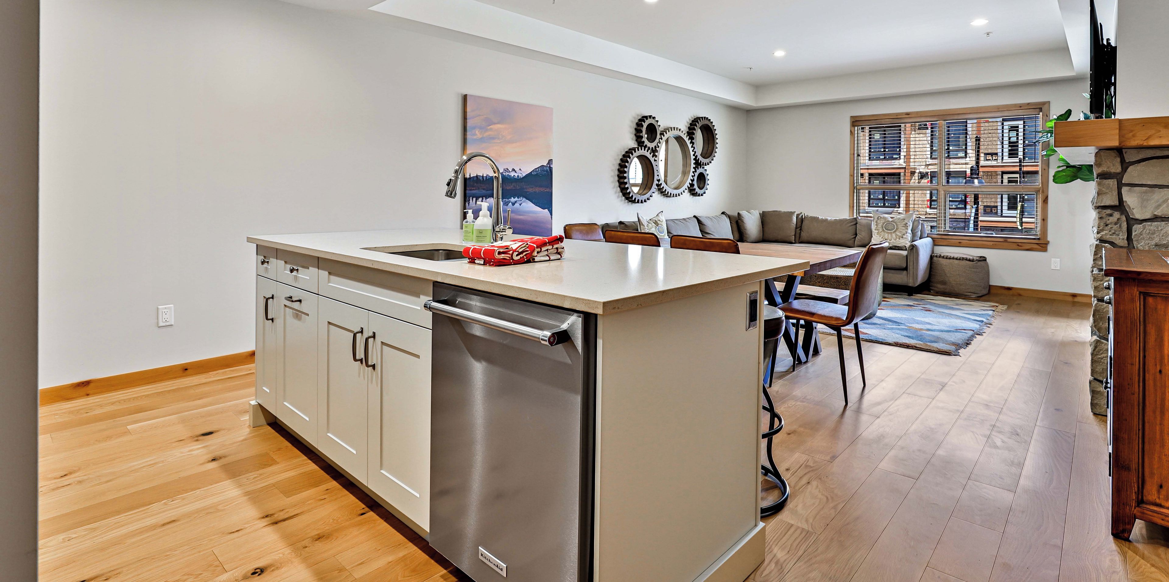 A spacious kitchen with a central island, a dining area with a wooden table and chairs, a stone fireplace, and a large window with a city view.