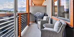 A balcony with wicker furniture, a grill, and a view of mountains.