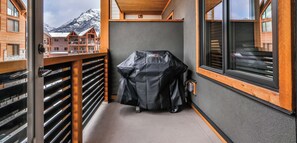 A balcony with a barbecue grill, wooden railings, and a view of a mountain.