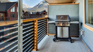Een balkon met een barbecue, houten reling en uitzicht op bergen.