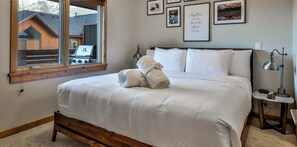 A neatly made bed with white linens and towels, a bedside lamp, and framed pictures on the wall.