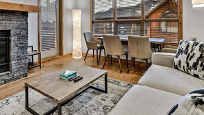 Una sala de estar moderna con chimenea de piedra, piso de madera, una mesa de centro, un sofá y un comedor con sillas.