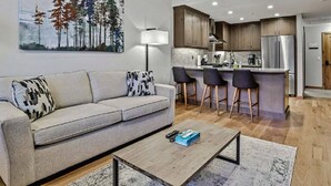 Una sala de estar moderna con un sofá, una mesa de centro y una zona de cocina con barra y asientos.