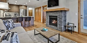 A modern living room with a stone fireplace, a sofa, and a coffee table. - Spring Creek Vacations 1 BR Elevated Condo 409W (Canmore)