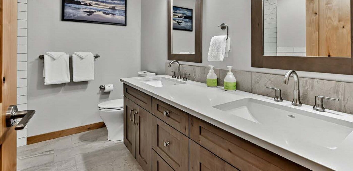 A modern bathroom with a double sink, wooden cabinets, a toilet, and two towels hanging on the wall.
