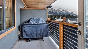 Un balcón con una parrilla cubierta, vista a montañas nevadas y barandilla de madera.