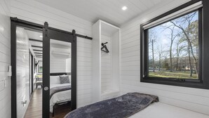 A bedroom with a bed, a window with a view of trees, and a sliding door leading to another room. - Brine Time: 2 mins to Lake Conroe! Heated Pool, Fire Pit, Stocked Ponds (Willis)