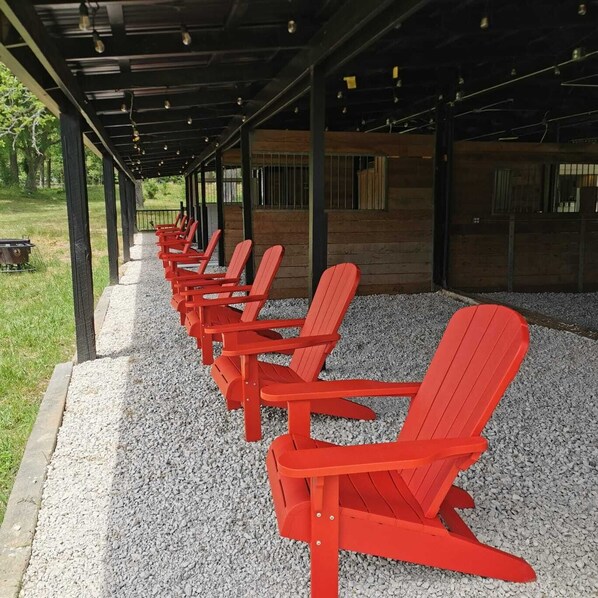 A covered outdoor seating area with red Adirondack chairs arranged in rows. - Hawg Boss: 2 mins to Lake Conroe! Heated Pool, Fire Pit, Stocked Ponds (Willis)