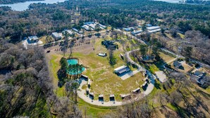 An aerial view of a resort with multiple buildings, a swimming pool, and a large body of water in the background. - Good Smoke -2 mins to Lake Conroe! Rooftop deck, Heated Pool, Fire Pit (Willis)