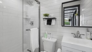 A modern bathroom with a glass shower enclosure, white tiled walls, a sink with a mirror, and a toilet. - Good Smoke -2 mins to Lake Conroe! Rooftop deck, Heated Pool, Fire Pit (Willis)