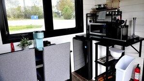 Ett kompakt kök med en kaffemaskin, mikrovågsugn och hyllor för förvaring.