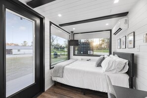 A bedroom with a bed, a TV, and a large window. - Low N' Slow -2 mins to Lake Conroe! Rooftop deck, Heated Pool, Fire Pit (Willis)