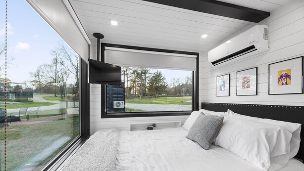 A modern bedroom with a large bed, a TV mounted on the wall, and a window overlooking a park.