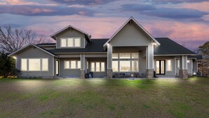 A two-story house with a large front porch, stone pillars, and a fire pit. - LUXURY home 2 mins to Lake Conroe! Heated Pool, Stocked Ponds, Cute Pygmy Goats (Willis)