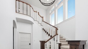 A grand staircase with a wooden handrail and white balusters, leading to a landing with a door. - LUXURY home 2 mins to Lake Conroe! Heated Pool, Stocked Ponds, Cute Pygmy Goats (Willis)