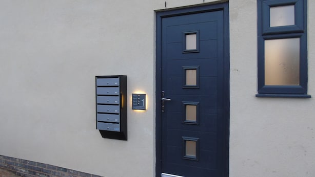 Une porte bleu foncé avec une boîte aux lettres et un luminaire fixé au mur.