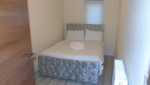 Une chambre à coucher avec un lit, une fenêtre avec des stores et un radiateur.